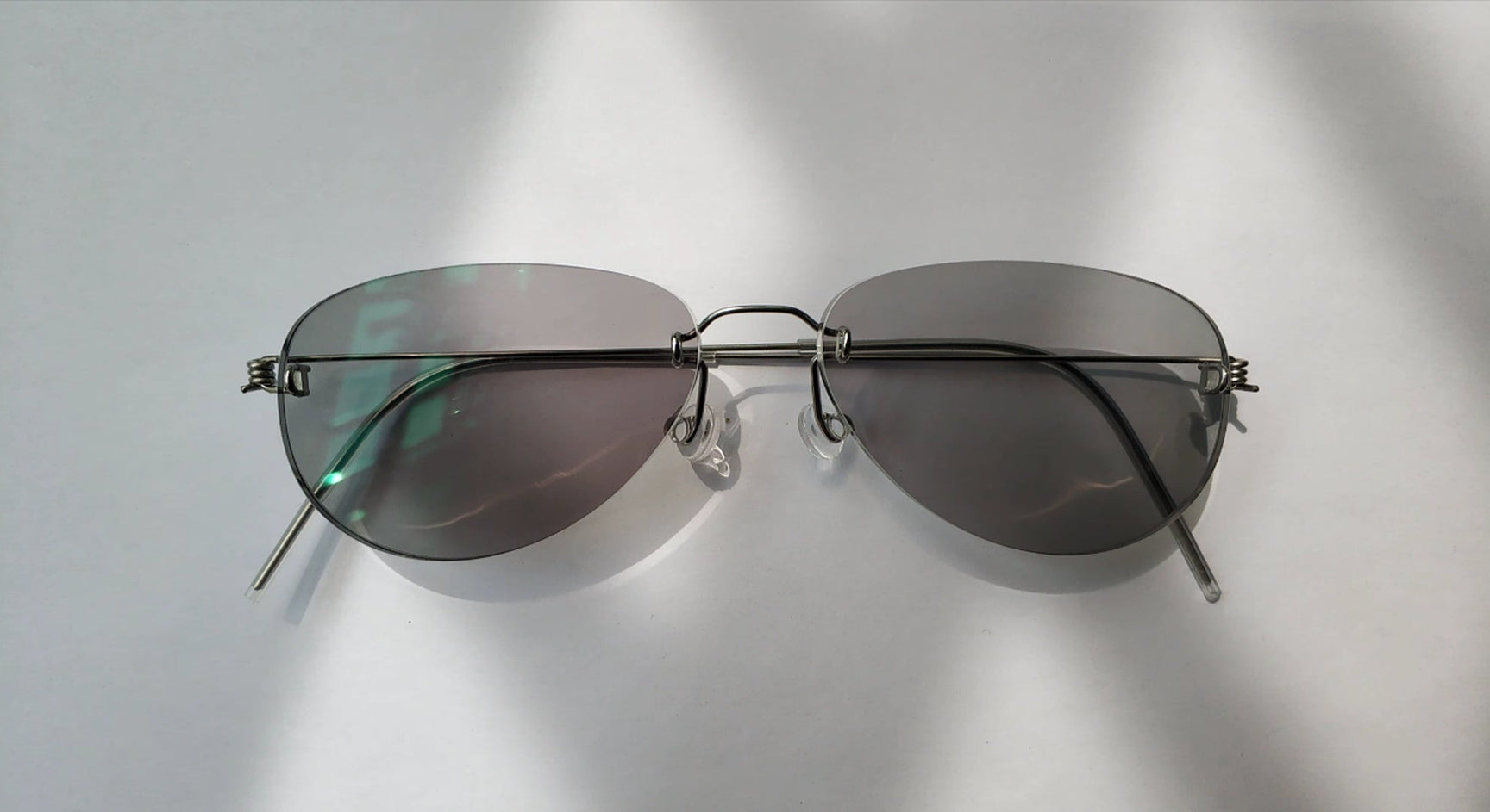 Yujo rimless custom stainless steel glasses folded on a white surface with soft shadow detail
